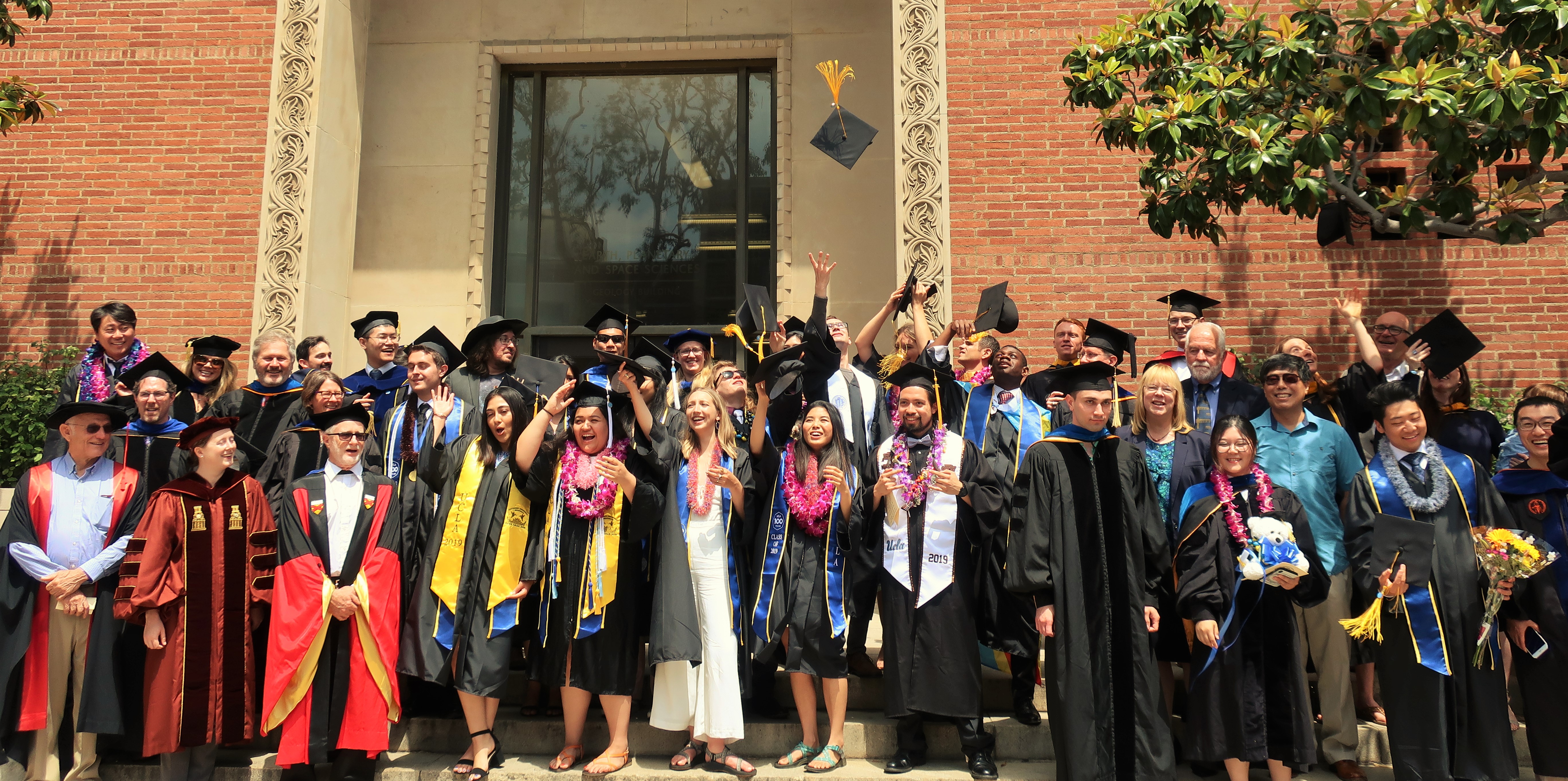 Image: Graduates and Faculty pose together on Geology Building steps, wearing regalia.