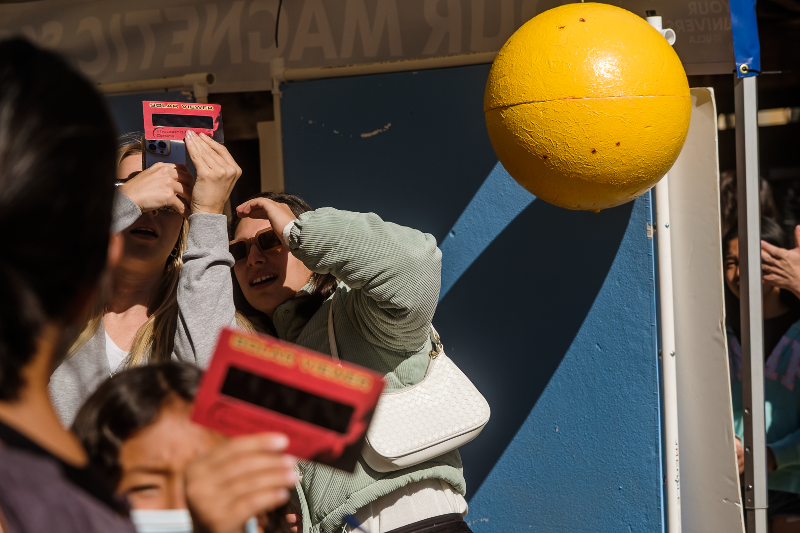 People hold handheld solar viewers in front of their eyes and look up at the sun.